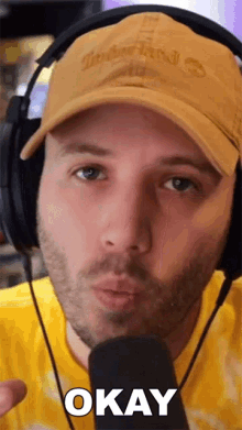 a man wearing headphones and a hat says okay in front of a microphone
