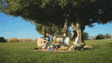 three women are having a picnic under a tree while one plays a guitar