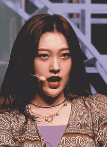 a close up of a woman 's face with a microphone in her mouth and a necklace with the letter s on it