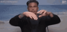 a man is making a heart shape with his hands while standing on a beach .