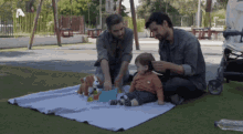 two men playing with a baby on a blanket