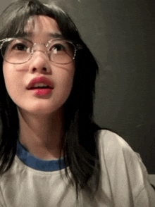a young woman wearing glasses and a white shirt is looking up .