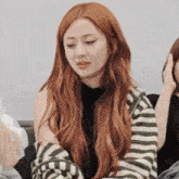 a woman with long red hair is wearing a striped sweater and a black shirt .