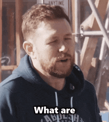 a man with a beard is wearing a blue hoodie that says " what are "