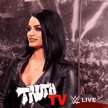 a woman in a leather jacket is sitting in front of a crowd and talking to someone .