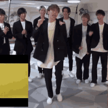 a group of young men are standing in a room and one of them is wearing a black jacket