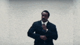 a man in a suit adjusts his tie while standing in front of a white wall