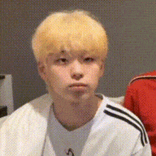 a young man with blonde hair is making a funny face while wearing a white shirt and a white jacket .