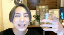a man is holding a glass of beer in front of a sign that says shots on it .