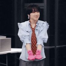 a woman wearing a tie and pink gloves stands with her hands folded
