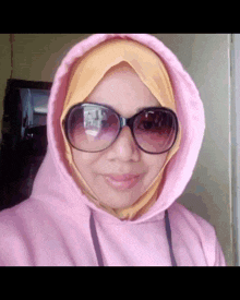a woman wearing a pink hoodie and sunglasses is smiling