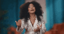 a woman with curly hair is making a funny face while wearing a white jacket and a necklace .