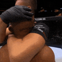 a man is hugging another man in front of a fence that says ' 9.com.sg ' on it