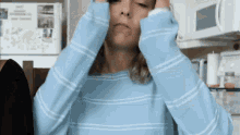 a woman wearing a blue and white striped sweater is covering her ears