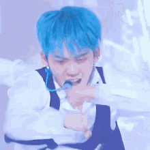 a man with blue hair and a microphone in his mouth is dancing on stage .