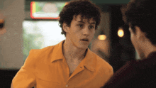 a young man in a yellow shirt is talking to another young man