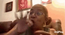 a woman with glasses is sitting on a couch and eating a piece of food .