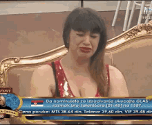 a woman in a red dress is sitting on a gold couch in front of a sign that says cena poruke