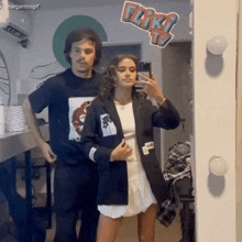 a man and a woman are taking a selfie in front of a mirror with a sticker that says fliki tv