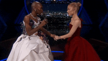 a woman in a white dress and a woman in a red dress are shaking hands