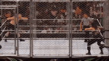 two wrestlers are fighting in a cage with a referee in the ring .