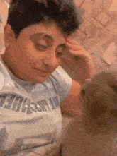 a young boy is sitting on a bed with a cat and scratching his forehead .