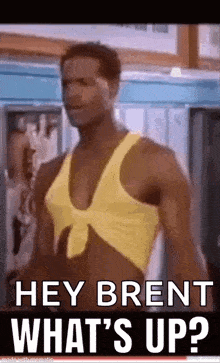 a man in a yellow tank top is standing in a locker room and saying `` hey brent what 's up '' .