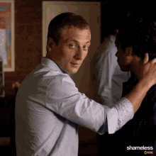 a man in a blue shirt is hugging another man in a shameless scene