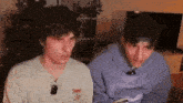 two young men are sitting next to each other in a living room and looking at something .