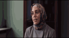 a woman wearing a hijab and a grey coat looks at the camera