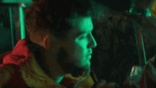 a man in a red jacket is sitting in a car with a yellow light behind him .