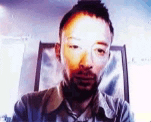 a man with a beard is looking at the camera with a blurry background behind him .