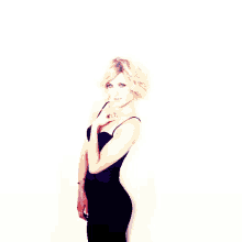 a woman in a black dress is standing against a white wall