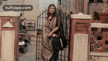 a woman is standing in front of a gate holding a bag and a purse .