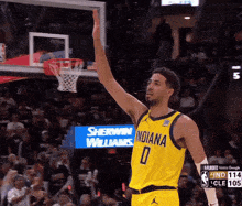 a basketball player wearing a yellow indiana jersey raises his arm in the air