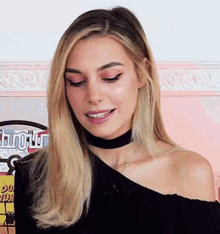 a woman wearing a black off the shoulder top and a choker smiles