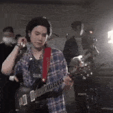 a young man in a plaid shirt is playing a guitar on stage .