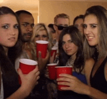 a group of people are holding red cups in their hands and looking at the camera