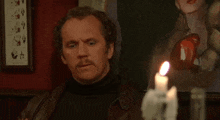 a man with a mustache is sitting in front of a lit candle in a dark room .