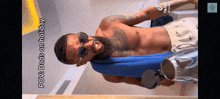 a shirtless man wearing sunglasses and a blue towel around his neck is standing in a room .