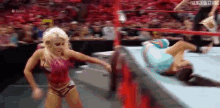 two women are wrestling in a wrestling ring and one is laying on the ground .