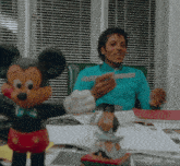 a man in a blue sweater is sitting at a desk with a mickey mouse toy in front of him