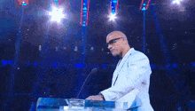 a man in a white suit is standing at a podium with a microphone in front of him .