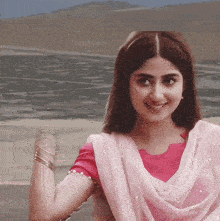 a woman wearing a pink top and a white veil smiles in front of a body of water