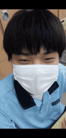 a boy wearing a blue shirt and a white face mask smiles