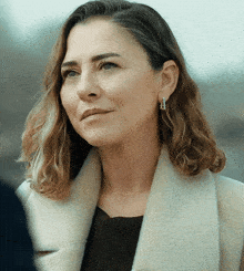 a woman wearing a white coat and earrings looks to the side