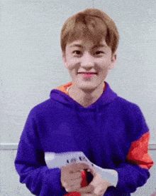 a young man in a purple hoodie is holding a piece of paper in his hands .