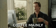 a man is drinking coffee while sitting at a desk in front of a computer monitor .