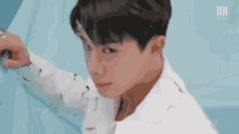 a young man in a white shirt is standing next to a blue wall and looking at the camera .