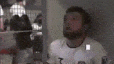a man with a beard is wearing a white shirt with the letter t on the front .